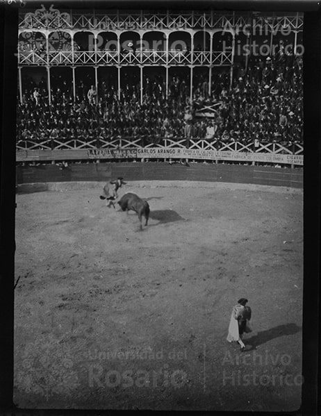 El entretenimiento público, a comienzos del siglo XX. El fotógrafo capturó el momento en que el toro embiste al torero, que casi que se eleva en el aire. Esta foto fue tomada en el Circo de Toros de San Diego, en Bogotá. La plaza de madera fue construida en 1904, nuevamente en 1915 y en 1917. La última construcción coincide con el escenario que aparece en la foto.